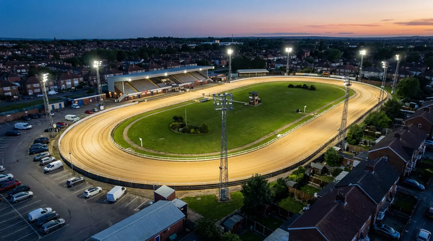 Aerial view of a UK greyhound racing stadium with sand oval track under floodlights